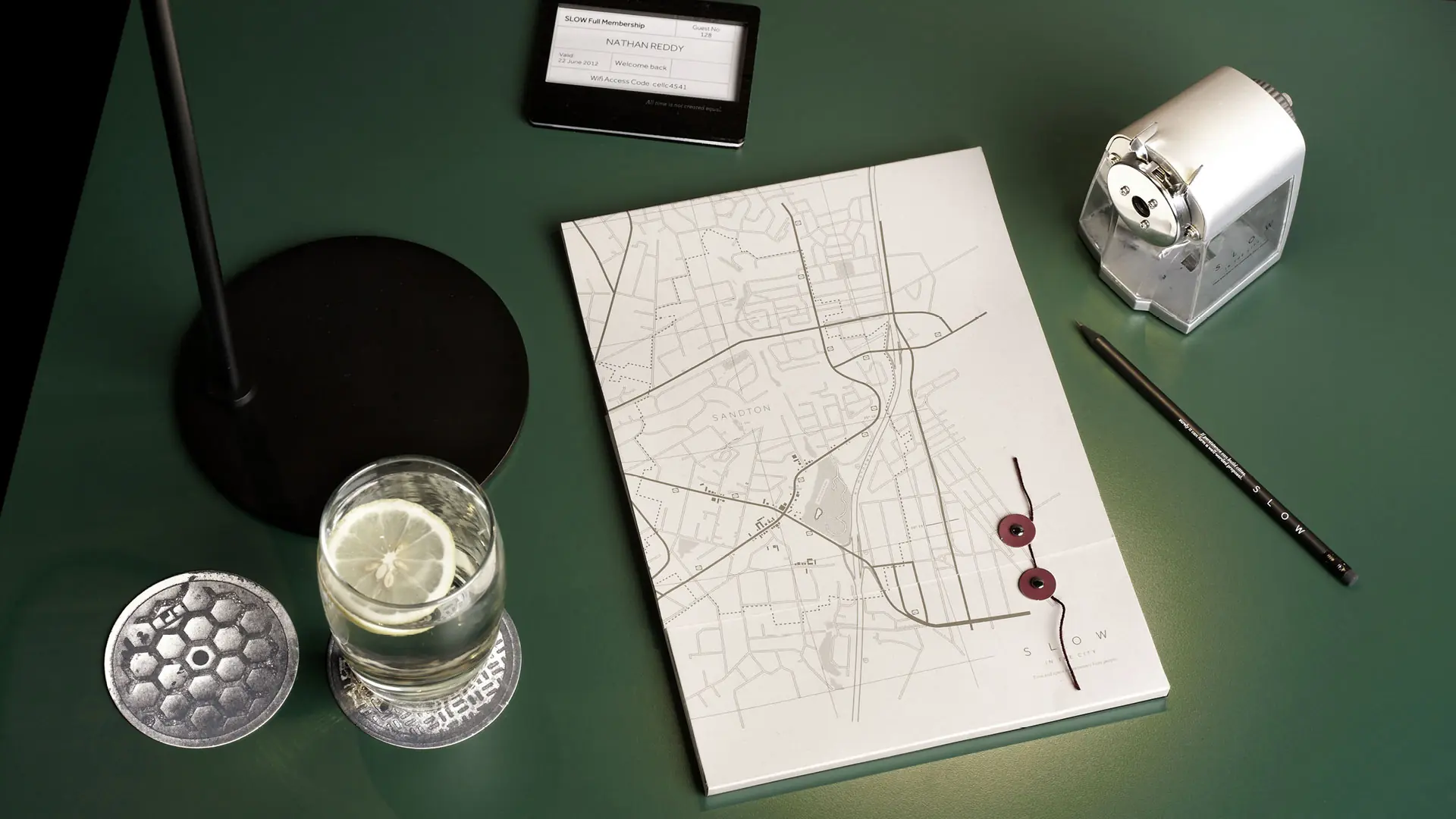 SLOW in the City map stationery, desk lamp and glass arranged on a deep green table