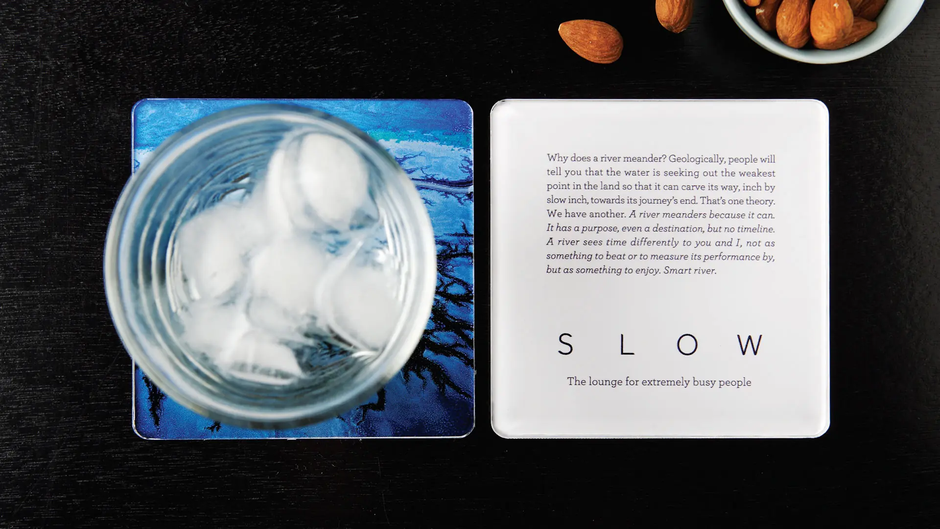 SLOW branded coaster paired with a glass of ice on a dark table