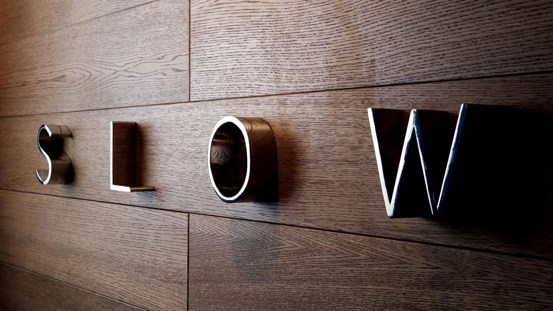 SLOW dimensional letterforms mounted individually against a warm timber wall