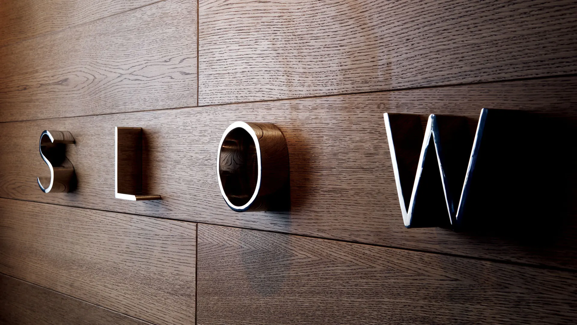 SLOW dimensional letterforms mounted individually against a warm timber wall